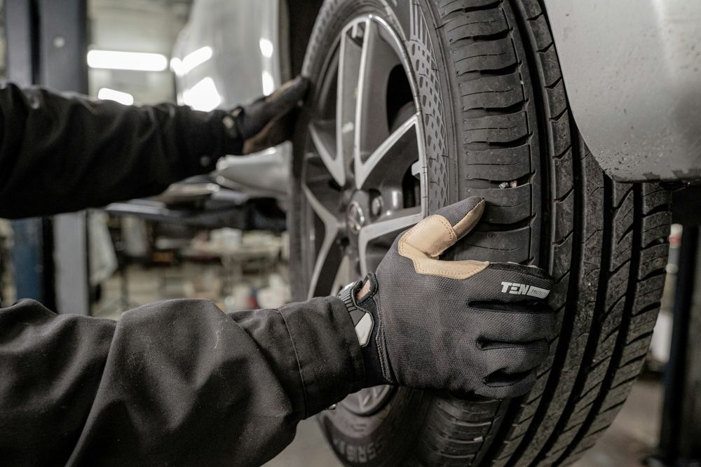 Gloved hands checking a tire on a car in a shop